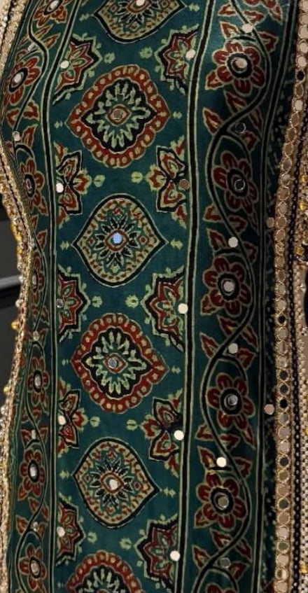 Close-up of an embroidered fabric panel with a dark teal background and intricate geometric and floral patterns in red, gold, green, and white, accented with small reflective mirror-like details.