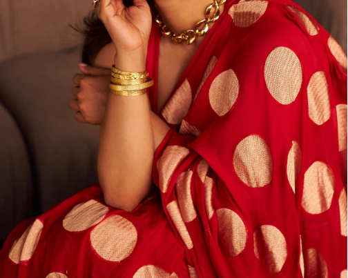 Red saree with gold polka dots worn by a person, accessorized with gold jewelry.