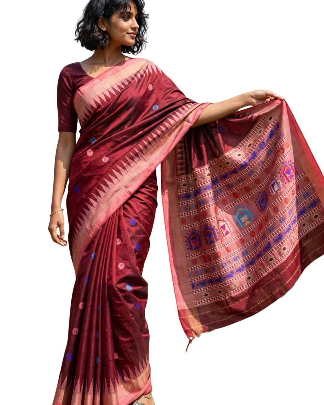 A woman modeling a deep maroon silk saree with a matching short-sleeve blouse. The saree features a pink and gold border with blue and pink geometric patterns on the pallu, and small blue and pink dots scattered along the body.
