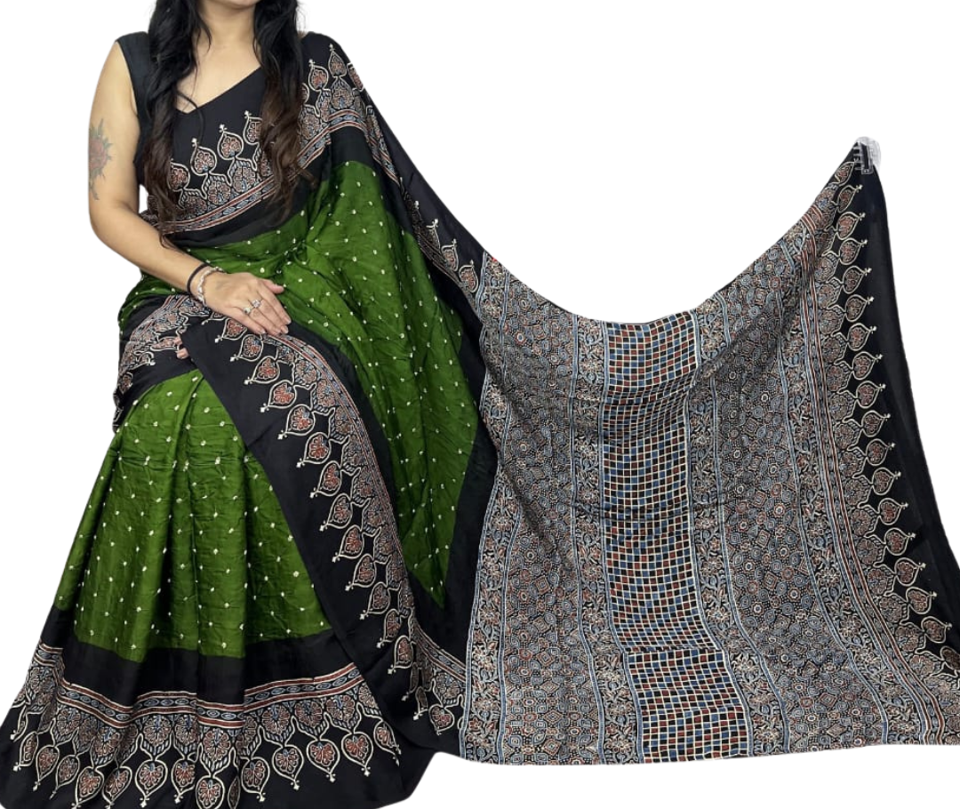 A woman models a green and black patterned saree with a matching black blouse against a plain white background. The saree features a solid green body with small white dots, a wide black border with intricate multicolor motifs, and a large black pallu with detailed geometric and floral patterns.