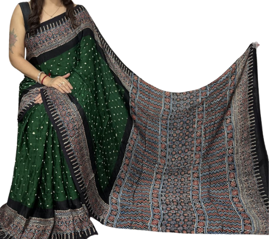 A woman models a dark green saree with small white dot patterns and a black border, while holding out a matching patterned dupatta with blue, red, and black geometric and floral designs on a plain white background.