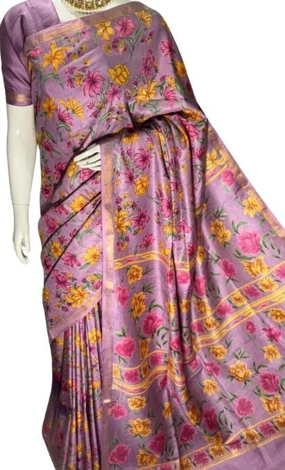 A lavender purple silk saree with a vibrant floral print in pink, yellow, and orange, displayed on a white mannequin against a white background.