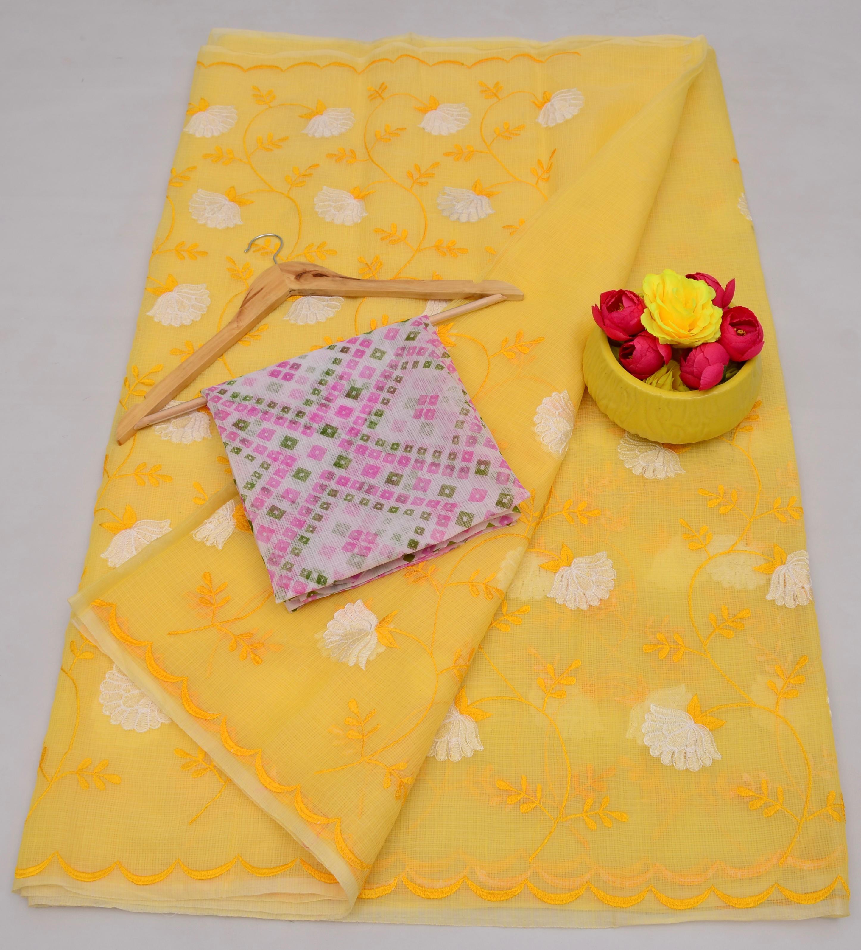 Yellow fabric with floral patterns, pink folded fabric, and yellow container with flowers on a light gray background