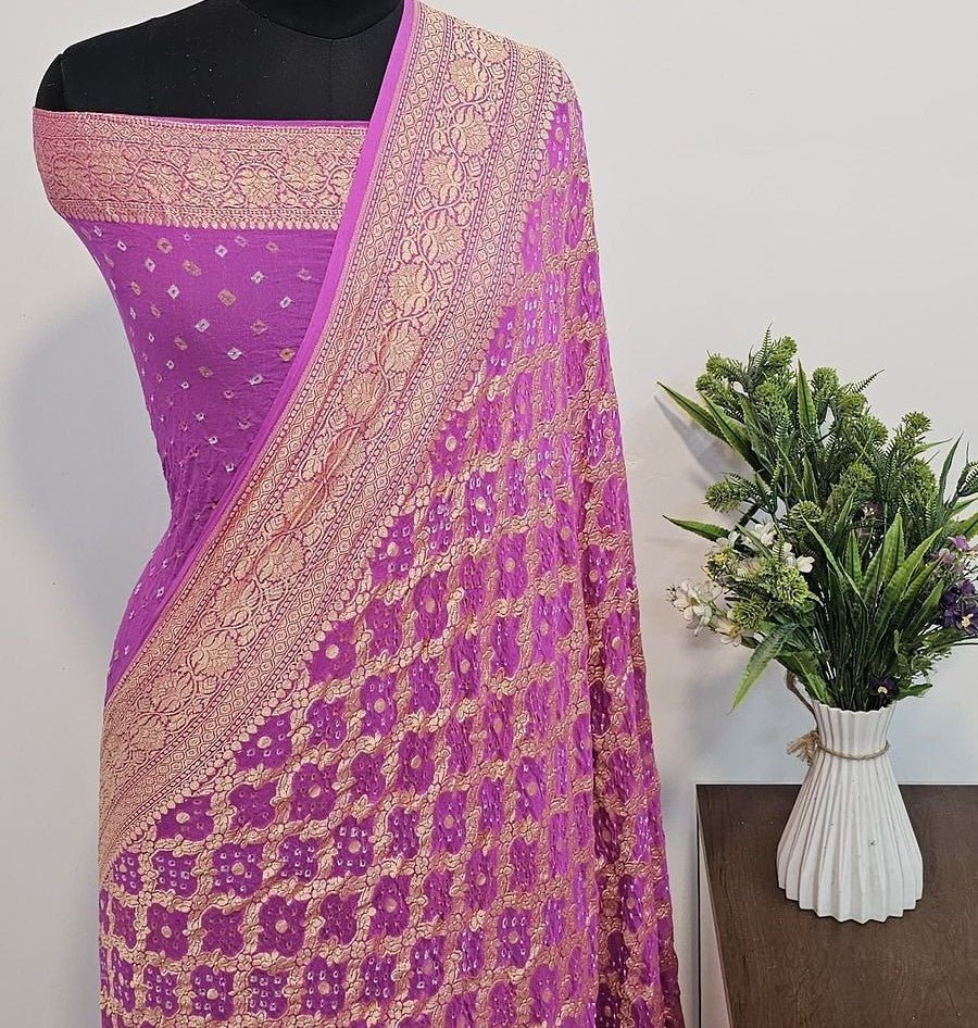 Purple saree with floral patterns on a mannequin, next to a vase of flowers on a wooden surface.