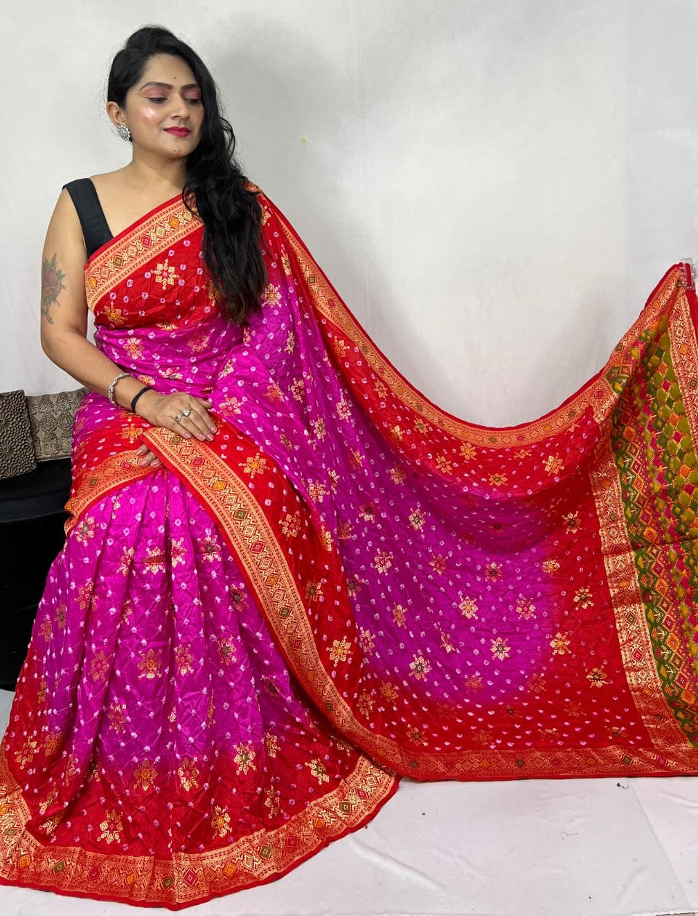 Woman wearing a vibrant red and pink saree with gold patterns on a white background