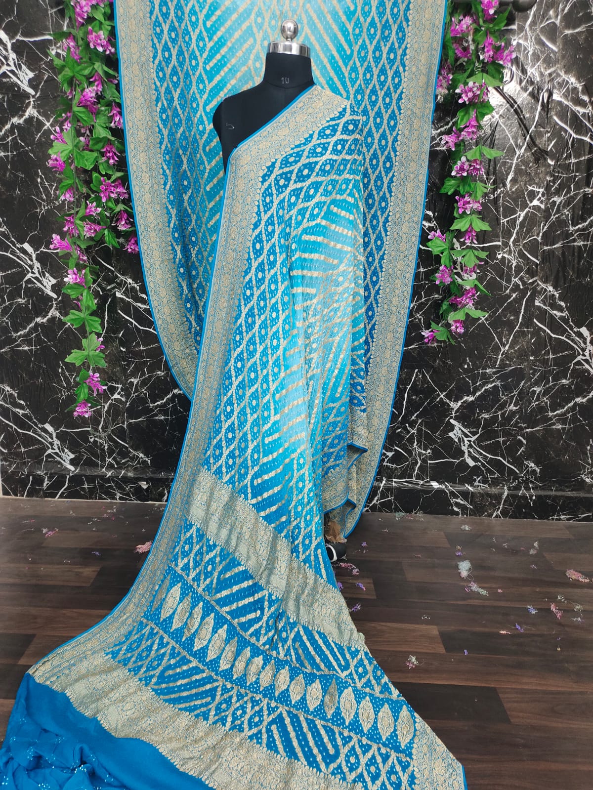 Blue and gray patterned fabric draped over a mannequin against a marble wall with purple flowers.