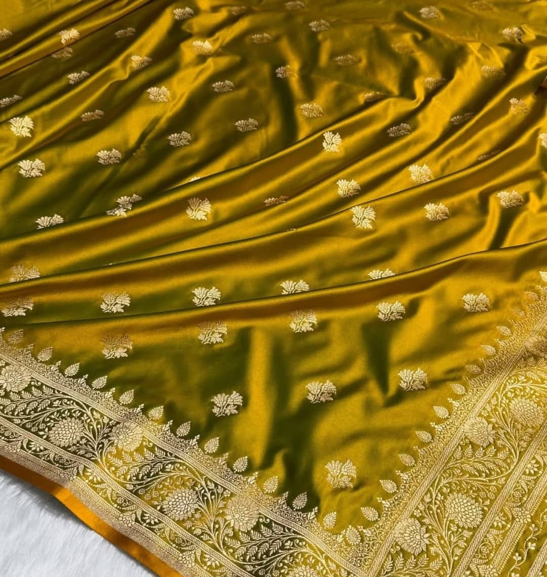 A close-up of a rich olive green Banarasi silk saree with intricate gold zari floral embroidery and a detailed gold border.