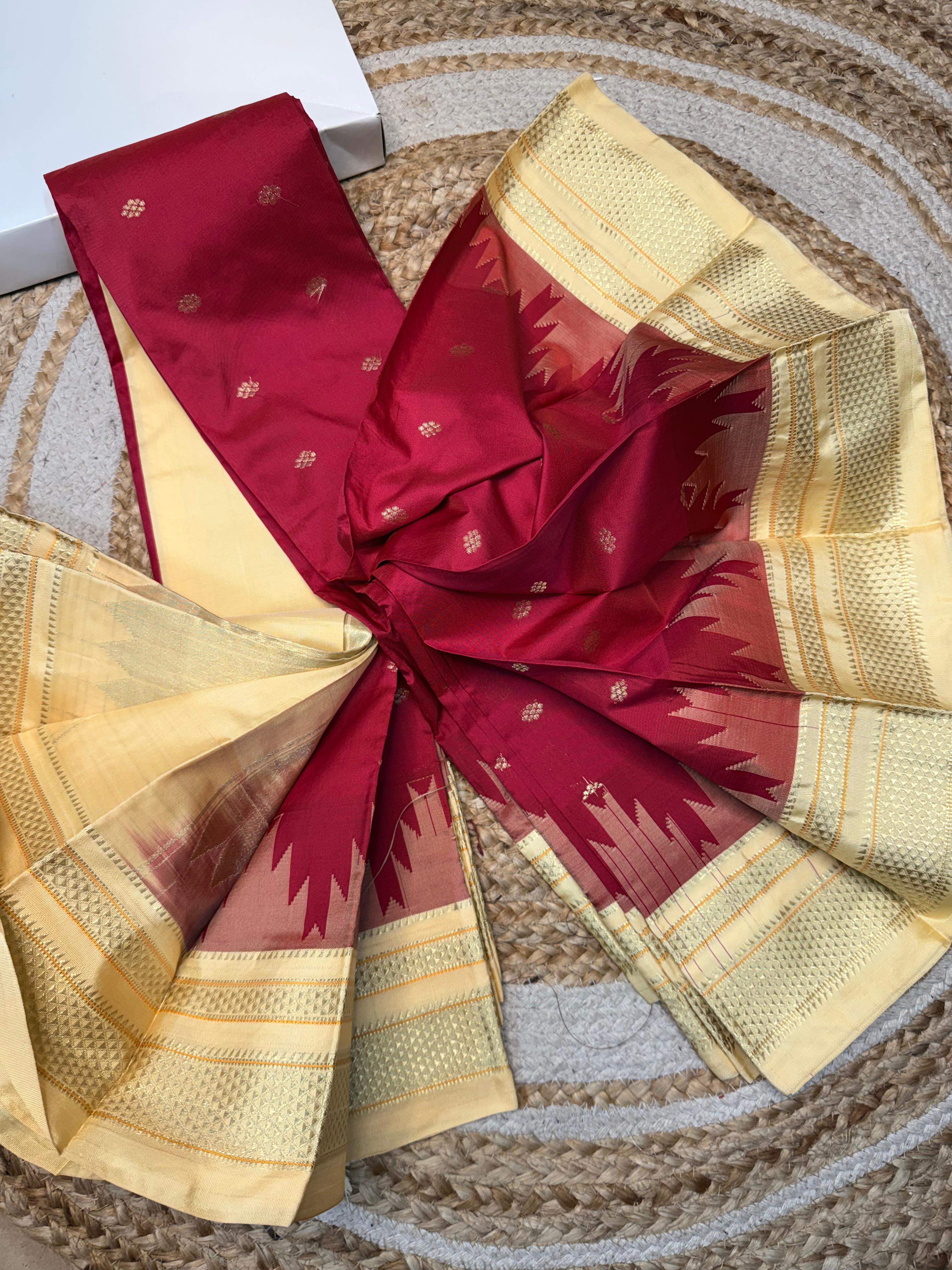 A folded and tied saree displayed on a woven round mat, featuring a deep red body with small gold motifs and a wide gold border.
