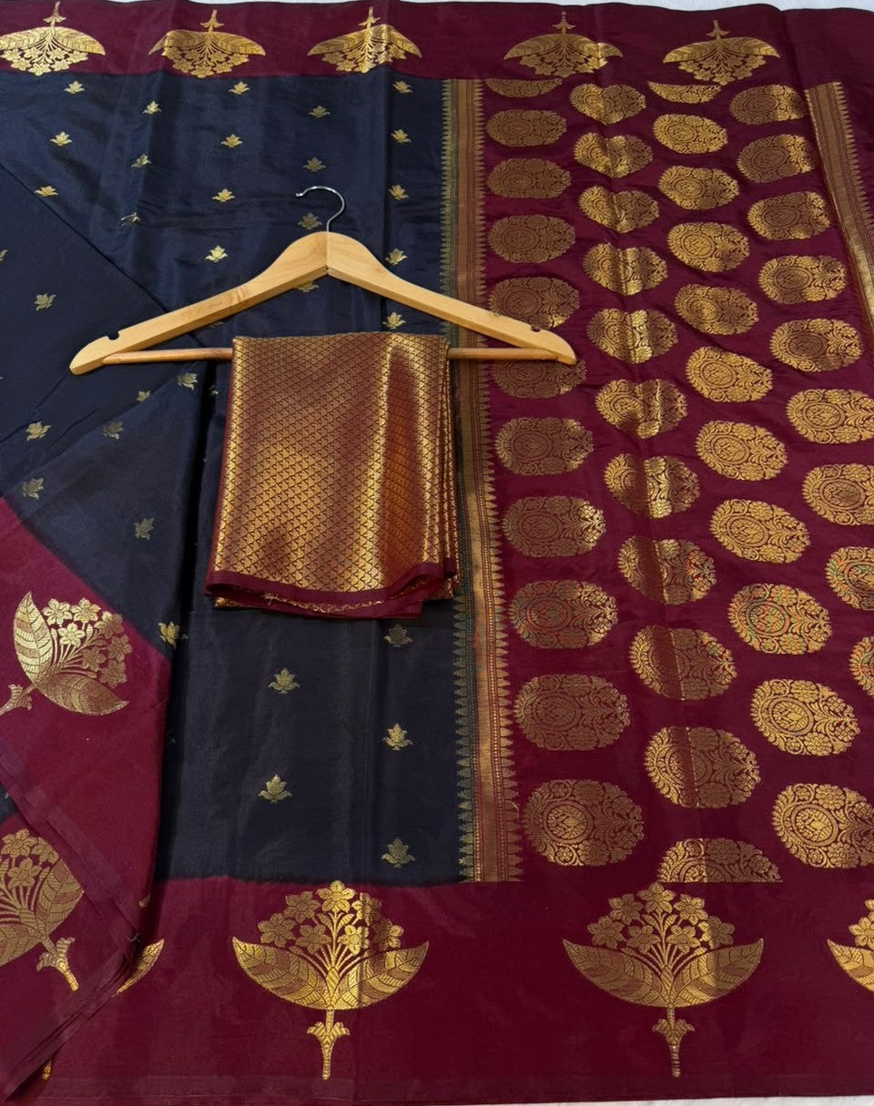 A dark navy blue and deep maroon silk saree with intricate gold zari woven patterns, displayed on a wooden hanger with a matching gold blouse piece.