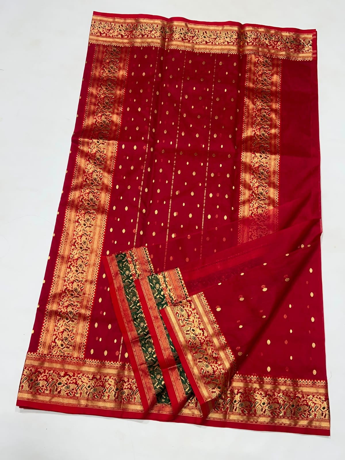 A red Banarasi silk saree with gold zari borders, gold polka dots, and a matching red and gold blouse piece folded on top, displayed on a white background.