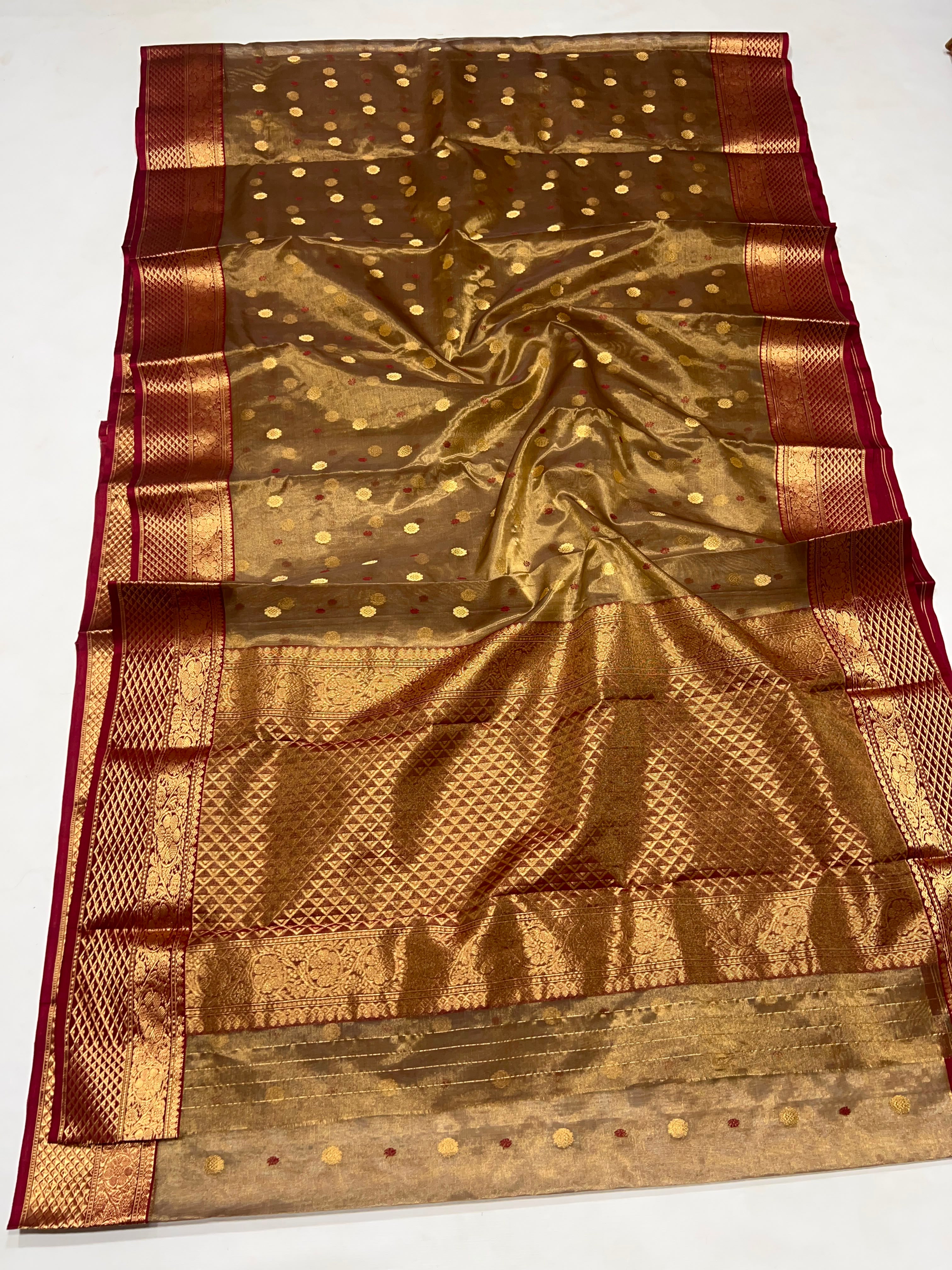 A traditional Indian silk saree with a metallic gold body, decorated with small gold dots, a wide red border, and intricate gold zari weaving.