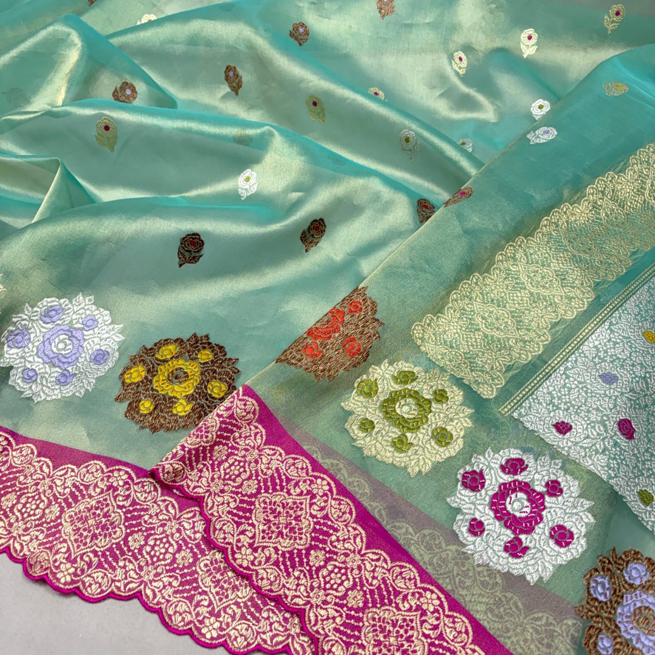A close-up of a mint green silk saree or fabric with scattered small floral motifs, a wide pink embroidered border, and a matching patterned pallu section.