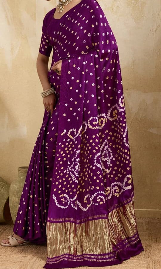 A purple Banarasi silk saree with white and gold tie-dye patterns and a gold zari border, modeled against a textured beige background.