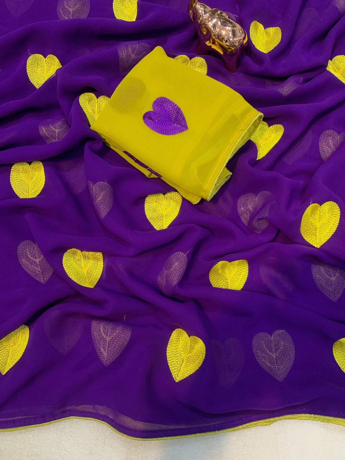Violet georgette saree fabric with yellow and purple heart motifs, featuring a folded yellow fabric piece with a purple heart patch on top.