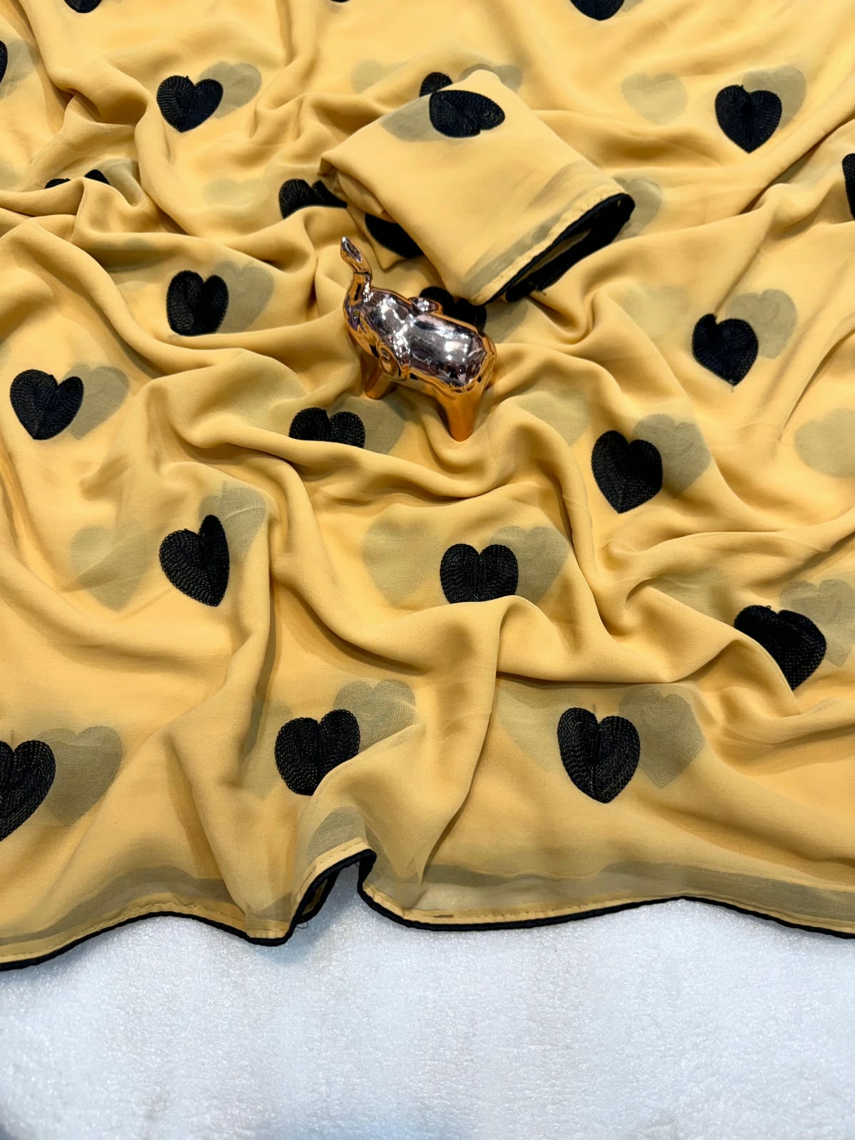 A draped beige fabric with a repeating black heart pattern, styled with a small metallic deer figurine on a white surface.
