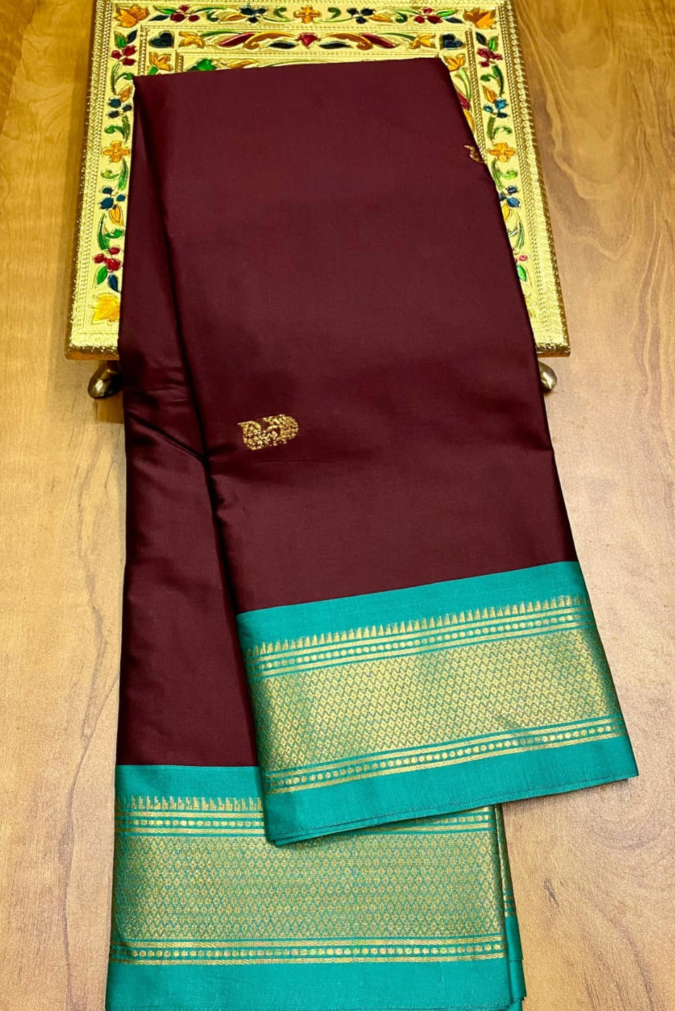 Maroon saree with green border on a wooden surface