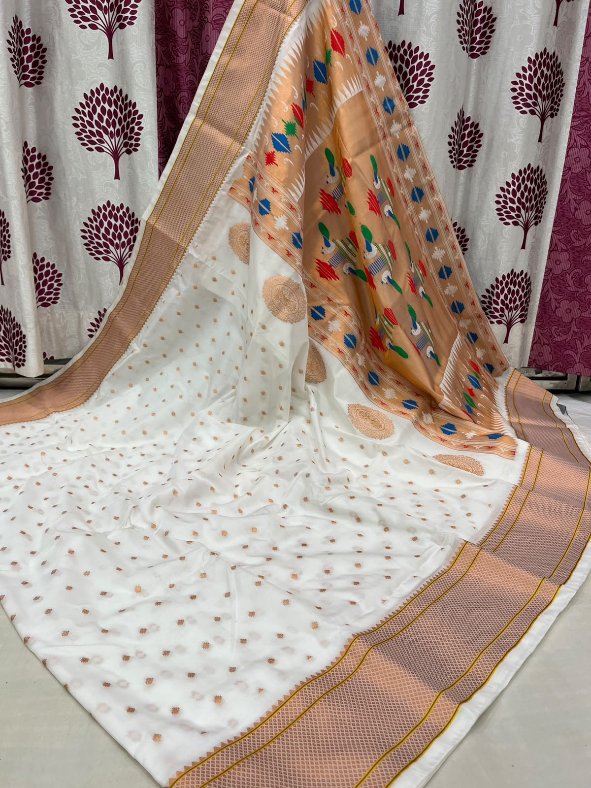 White saree with a brown border and colorful patterns on a plain background