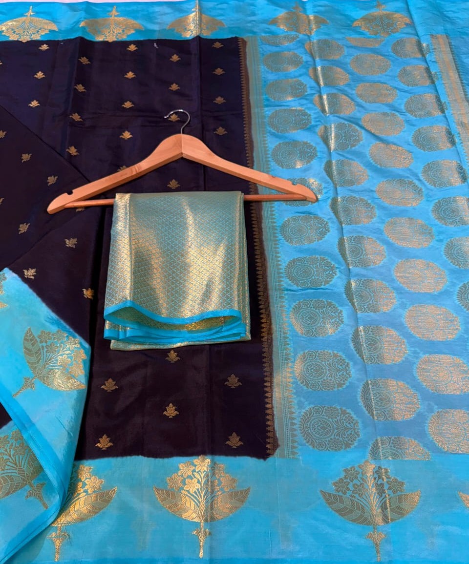 A blue and black silk saree with gold zari brocade work, displayed on a wooden hanger with a matching folded blouse piece.
