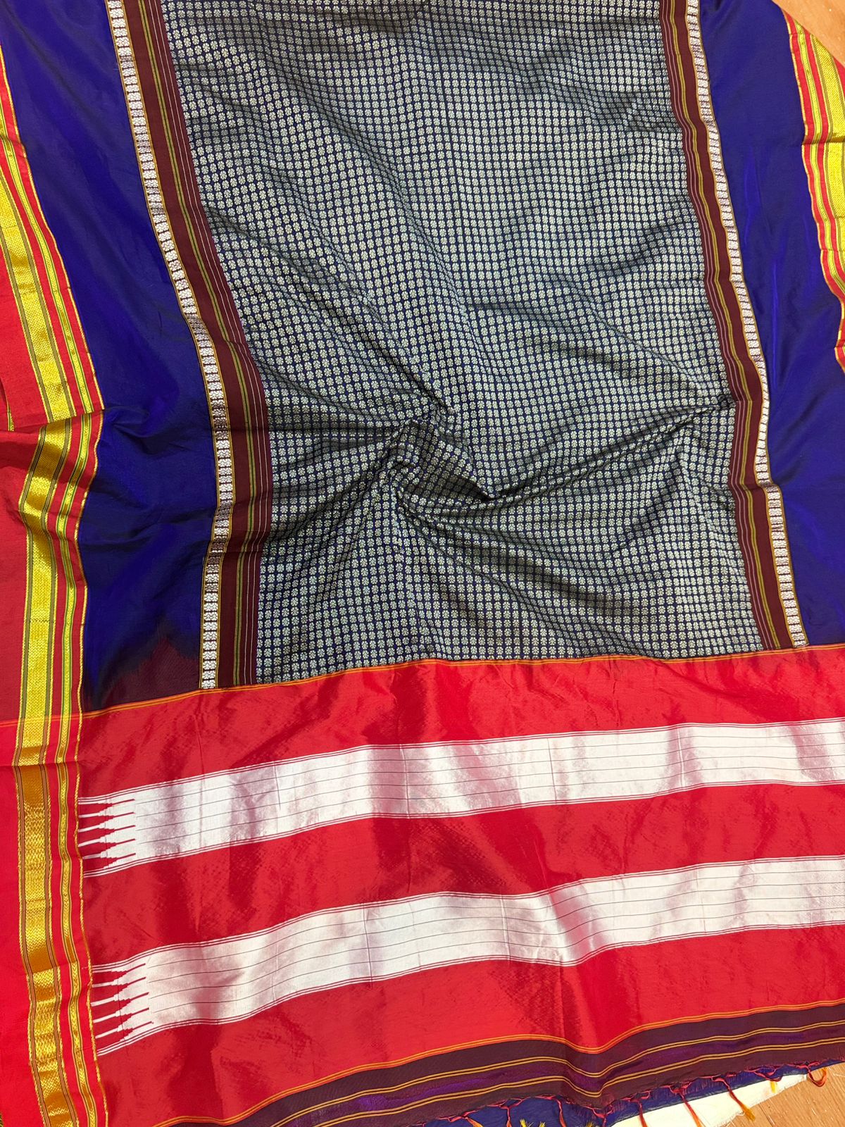A close-up of a traditional Indian saree fabric, showing the black and white checkered body, the royal blue pallu with gold and red borders, and the red and white striped border.