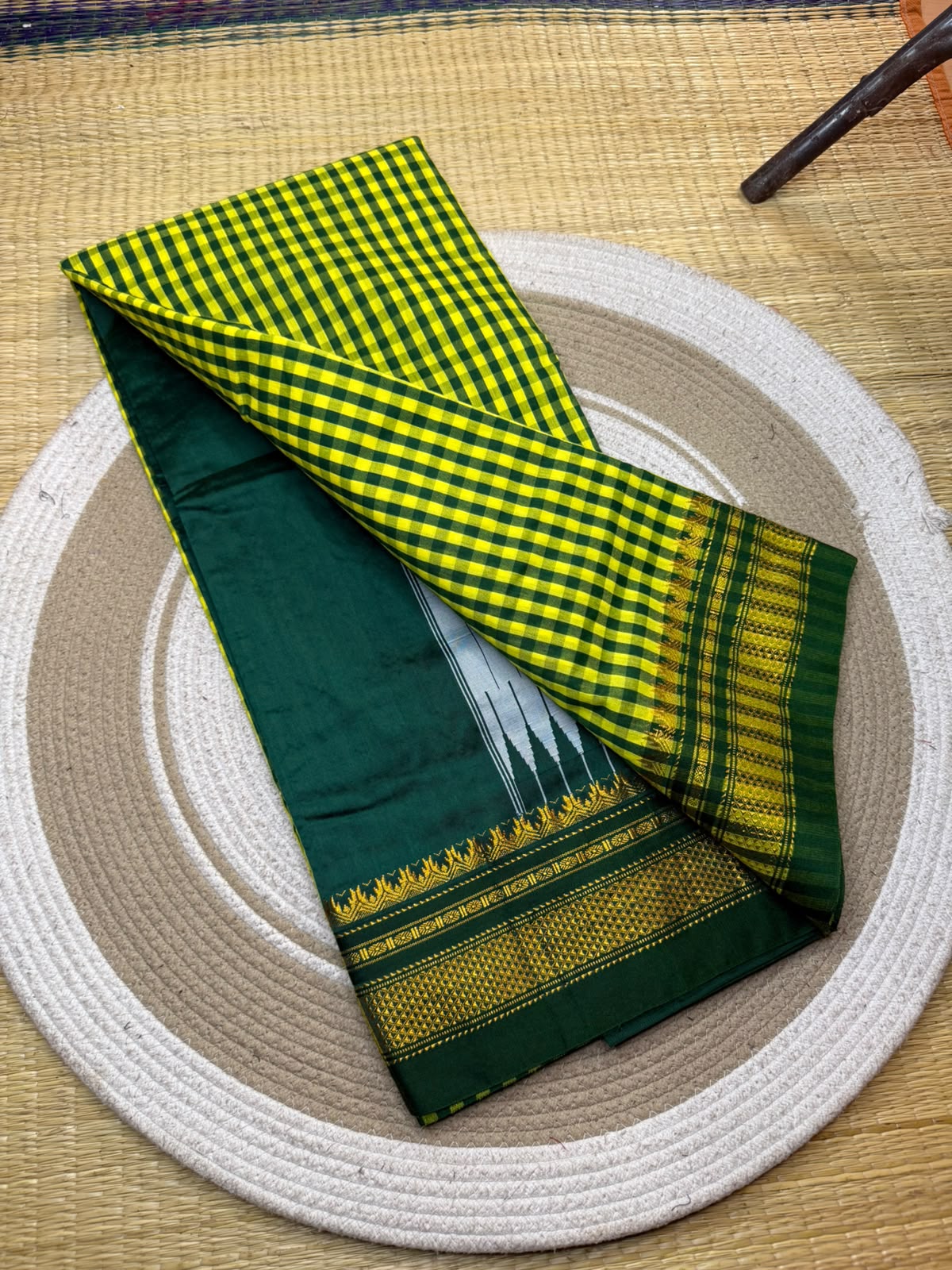A folded green and yellow checkered saree or fabric piece with a dark green border and gold patterned edge, displayed on a round woven mat.