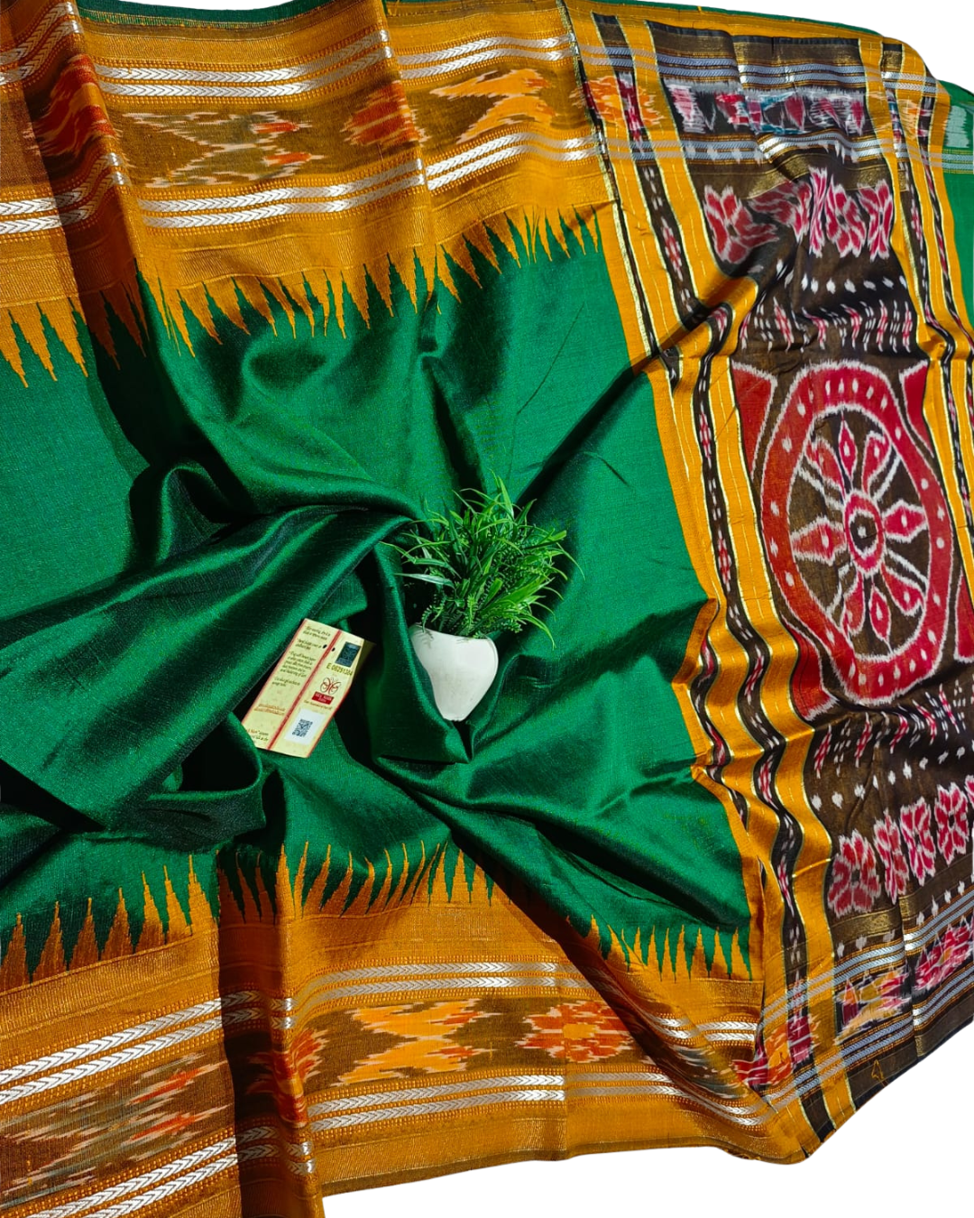 Green and orange traditional fabric with patterns, a plant, and a small box on a white background