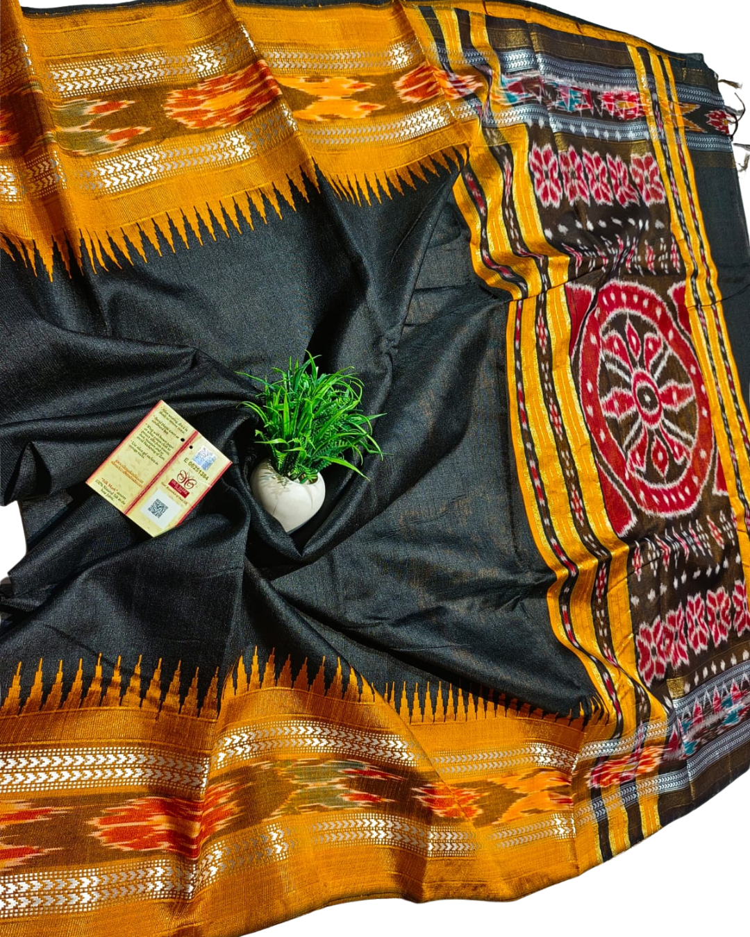 Black saree with colorful patterns and a plant on a white background