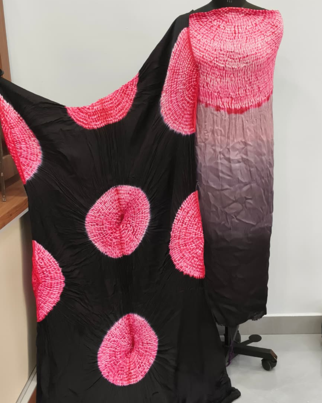 Black dress with pink circular patterns on a mannequin against a white wall.