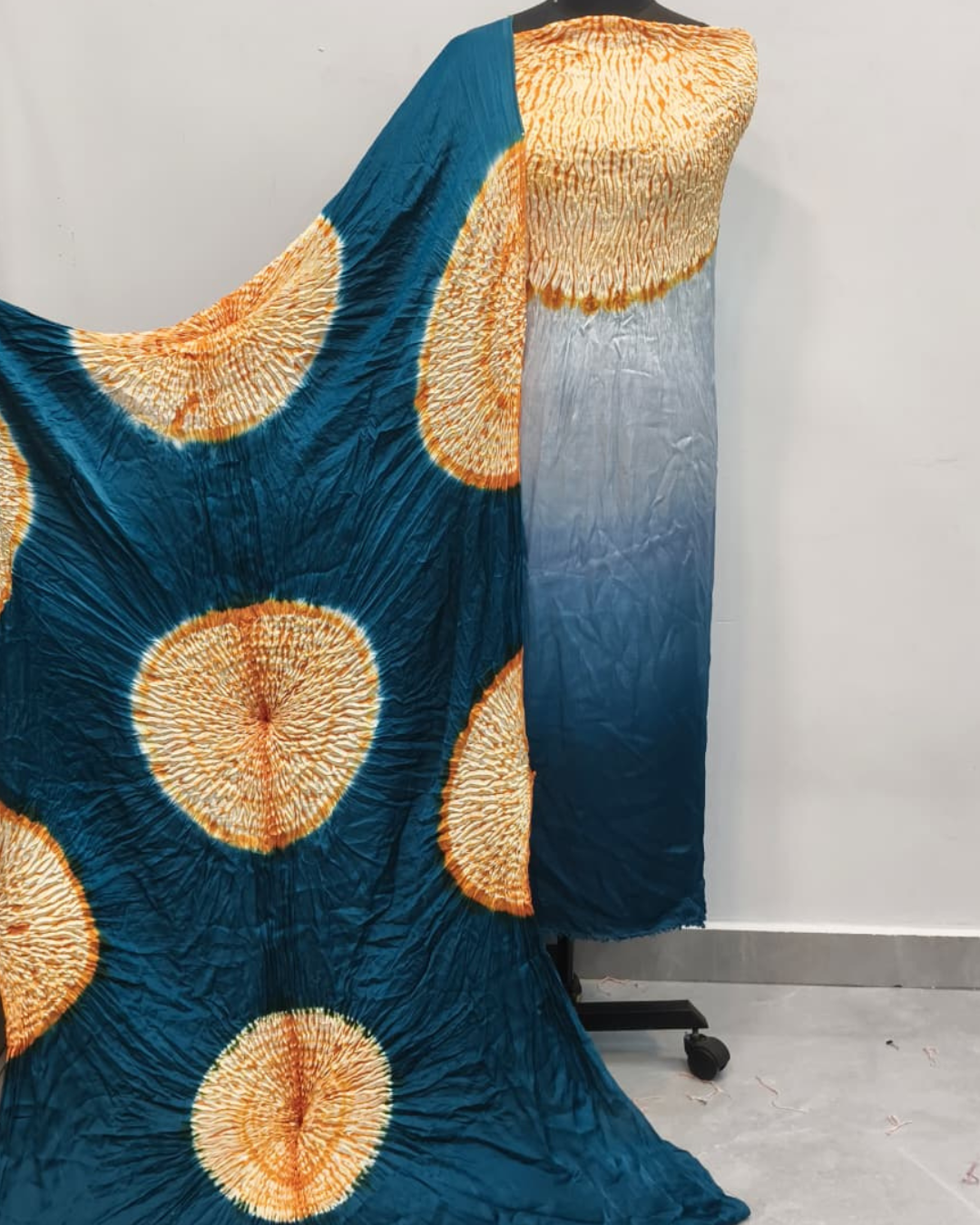 Textile with blue and gold pattern draped over a stand against a gray background