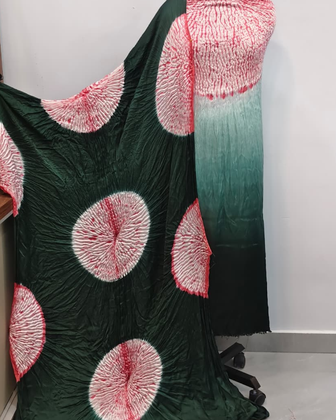 Green fabric with red circular patterns on a mannequin against a white background