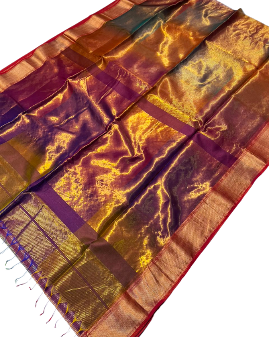 A metallic gold and purple silk saree with a red border, laid out diagonally on a white background.