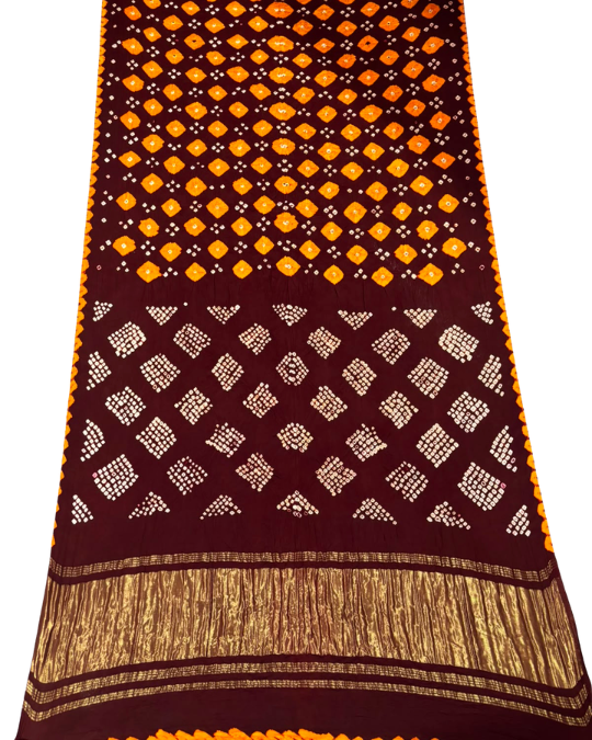 A dark maroon Bandhani fabric with orange and white tie-dye patterns, featuring a wide gold metallic border at the bottom.