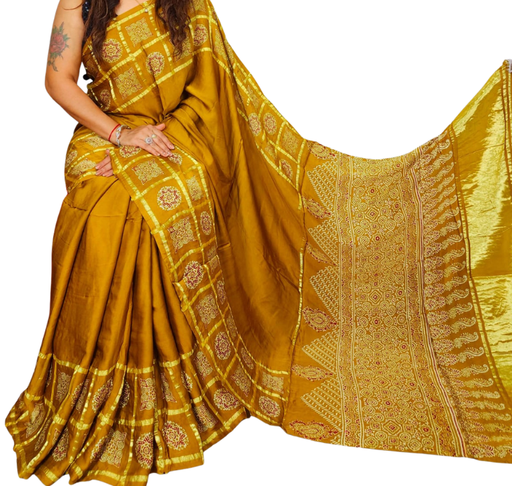 A woman models a mustard yellow silk saree with intricate gold and silver zari embroidery, featuring a wide border and a matching dupatta, set against a plain white background.